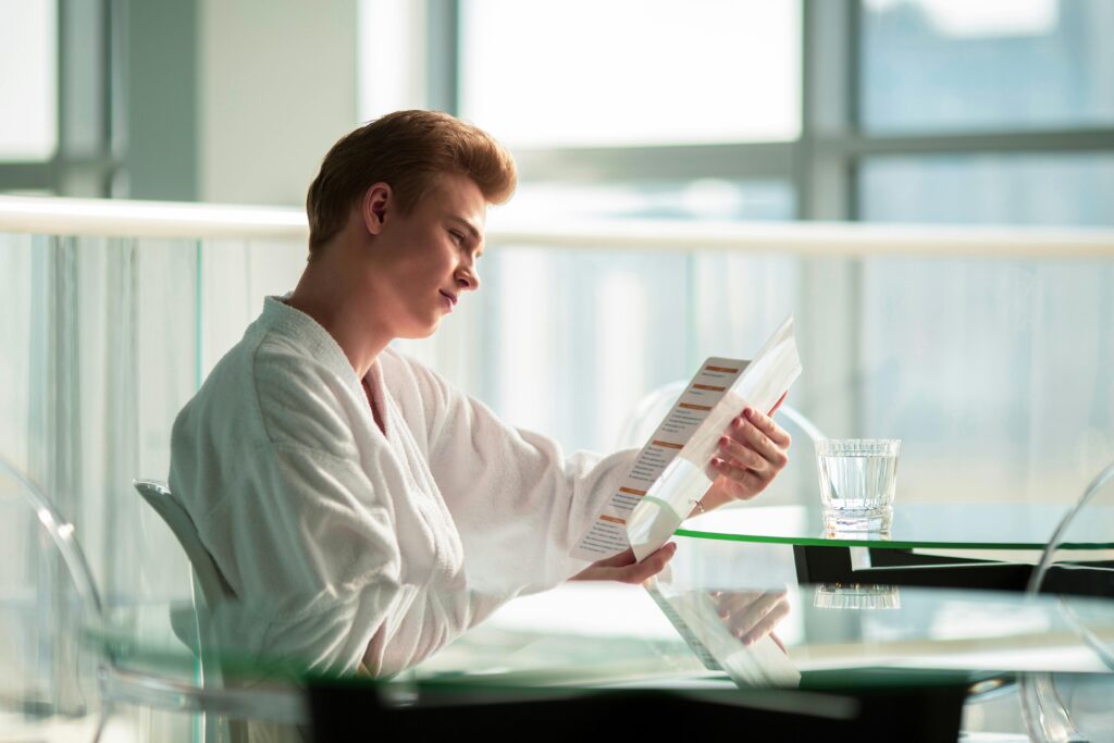 Man in a bathrobe reading a menu at a hotel lounge glass table with refreshing ambiance.